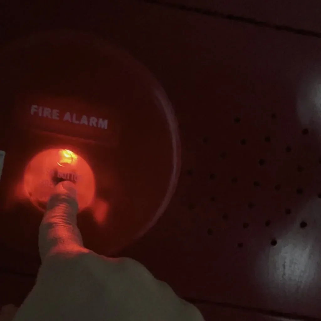 Ngón tay bấm nút ấn báo cháy FIRE ALARM màu đỏ đang sáng đèn