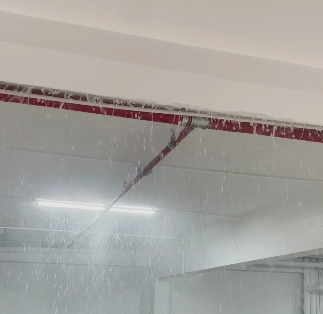 Nước xả từ đầu phun sprinkler trên đường ống chữa cháy sơn đỏ dưới trần tầng để xe khi chạy thử hệ thống chữa cháy tự động