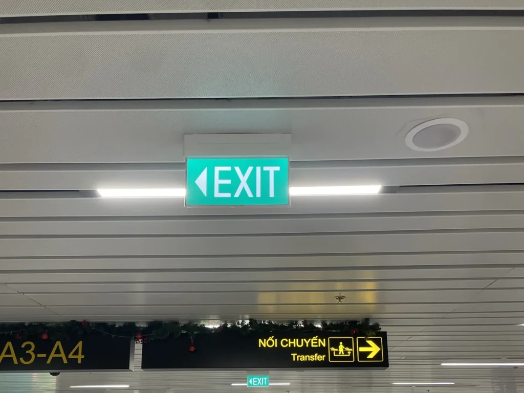 Đèn EXIT chỉ dẫn lối thoát nạn có mũi tên chỉ hướng, treo trần hành lang nhà ga