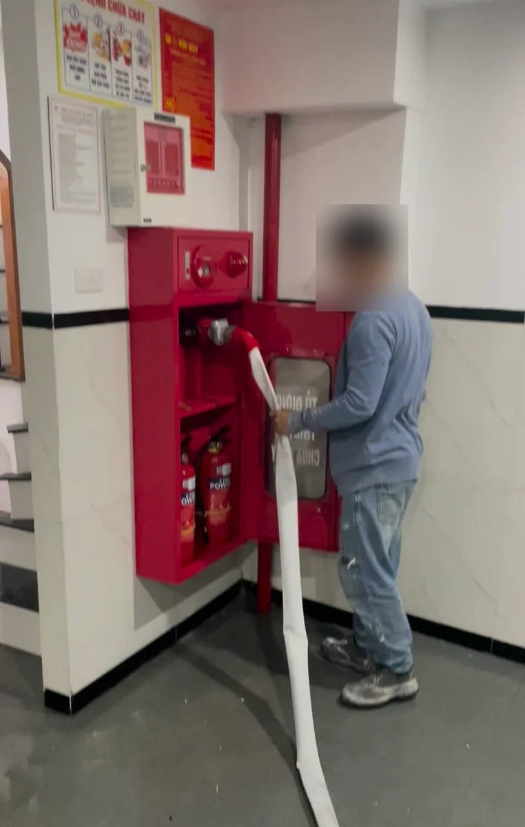 Người kéo vòi chữa cháy từ hộp chữa cháy vách tường sơn đỏ ở sảnh cầu thang một nhà nhiều tầng để thử phun nước