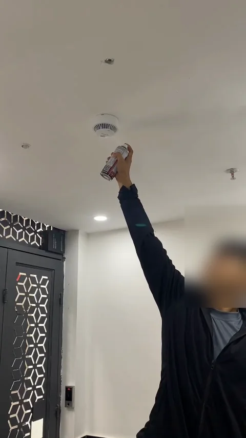Kỹ thuật viên giơ bình xịt khói thử lên đầu báo khói gắn trần để thử hệ thống báo cháy