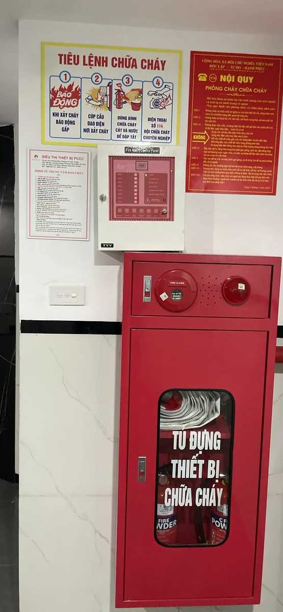Tủ trung tâm báo cháy gắn tường phía trên hộp đựng thiết bị chữa cháy có chuông, đèn, nút ấn báo cháy, bên cạnh tiêu lệnh và nội quy phòng cháy chữa cháy