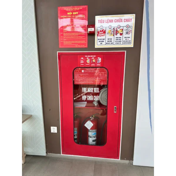 Tủ chữa cháy sơn đỏ lắp lọt trong hốc tường, mặt cửa ngang mặt tường, bên trong có cuộn vòi và bình chữa cháy
