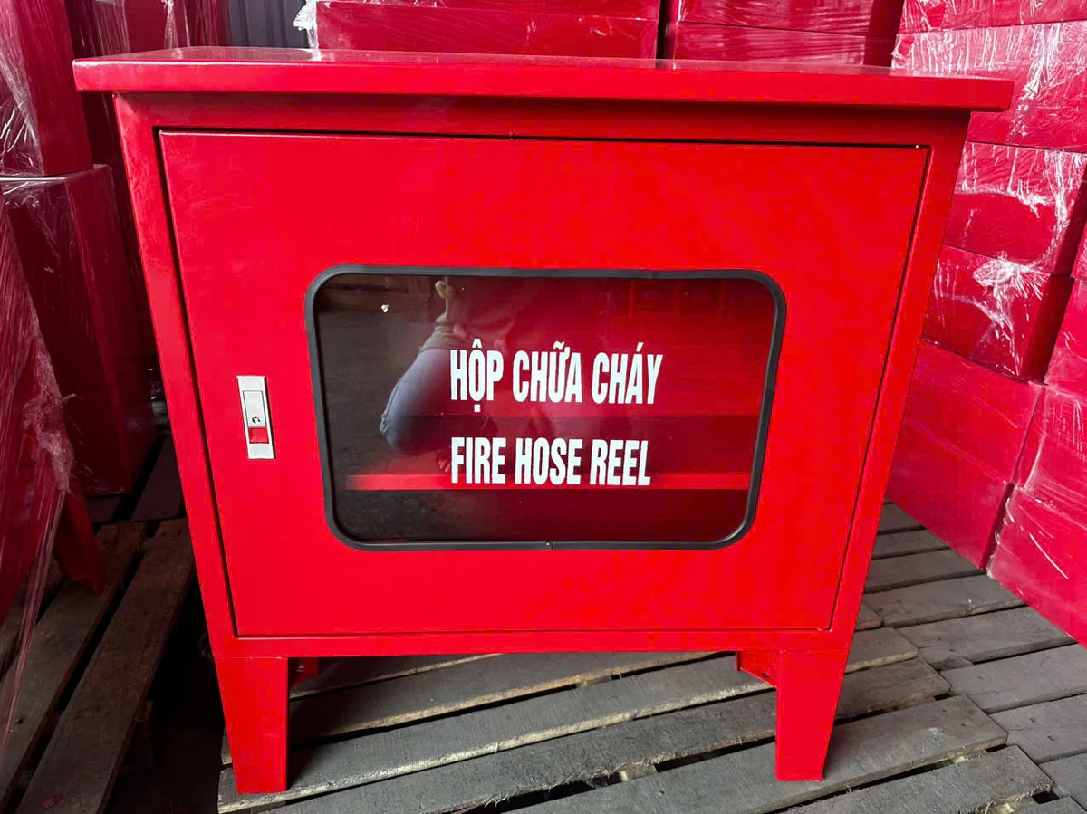 Tủ chữa cháy ngoài trời sơn đỏ có bốn chân cao, cửa kính ngang ghi Hộp chữa cháy, đặt tại kho