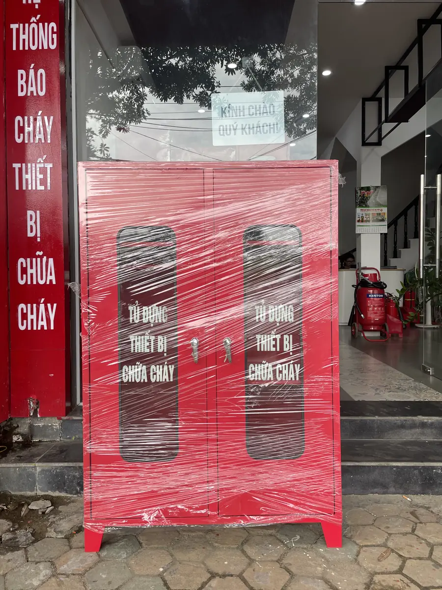 Tủ đựng thiết bị chữa cháy 2 cánh màu đỏ có ô kính, còn bọc màng nilon, đặt trước cửa hàng thiết bị PCCC