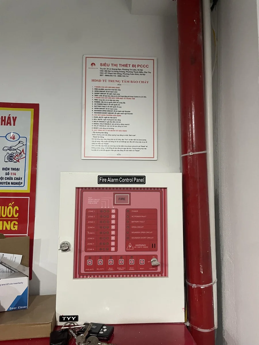 Tủ trung tâm báo cháy lắp đặt tại công trình, phía trên có bảng hướng dẫn vận hành tủ, bên cạnh đường ống chữa cháy